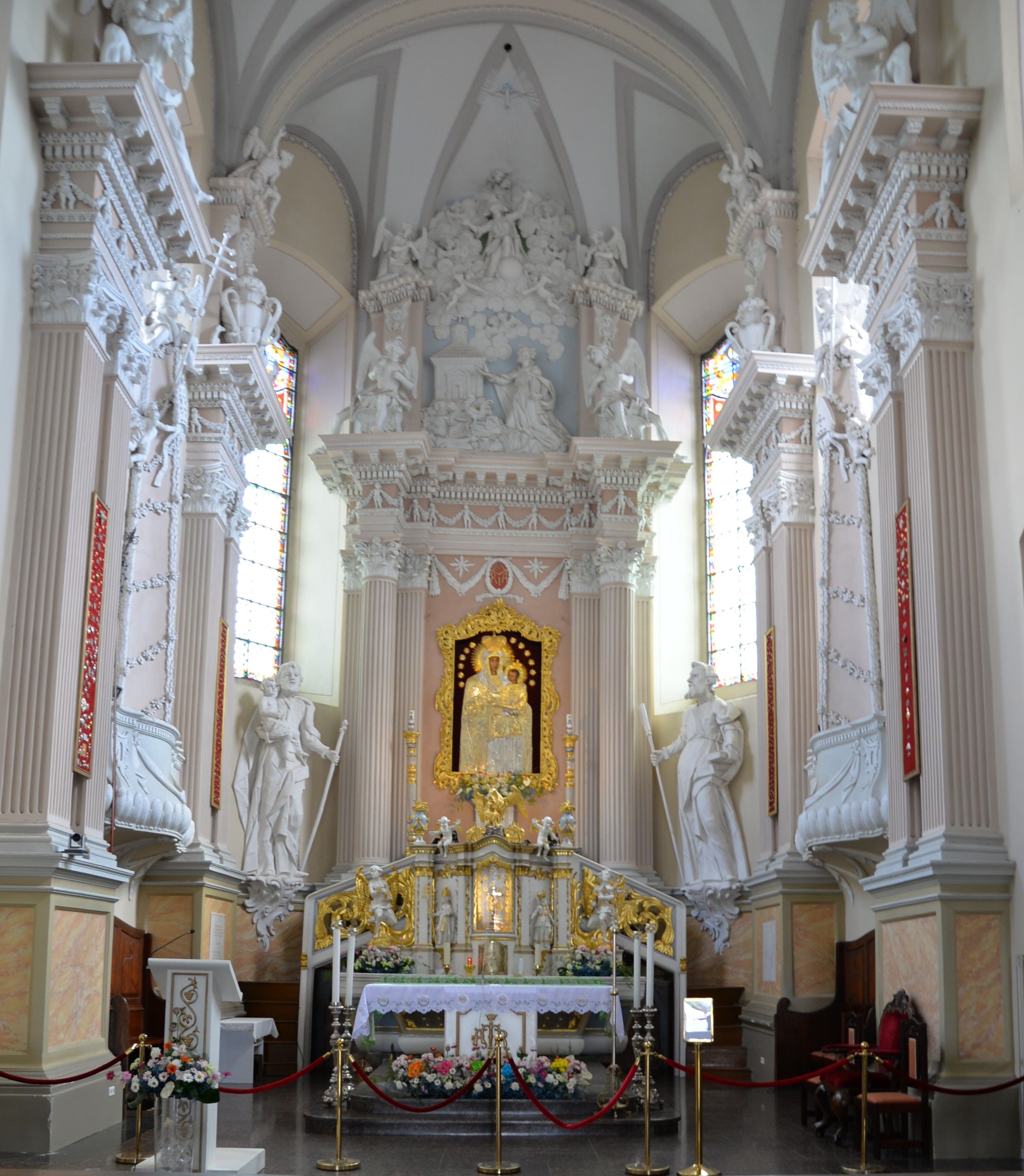 Intérieur de l'église de la Visitation de la Bienheureuse Vierge Marie à Szydłów, avec un autel richement décoré et une image encadrée en or de la Vierge Marie et l'Enfant, entourée de statues blanches et de colonnes.