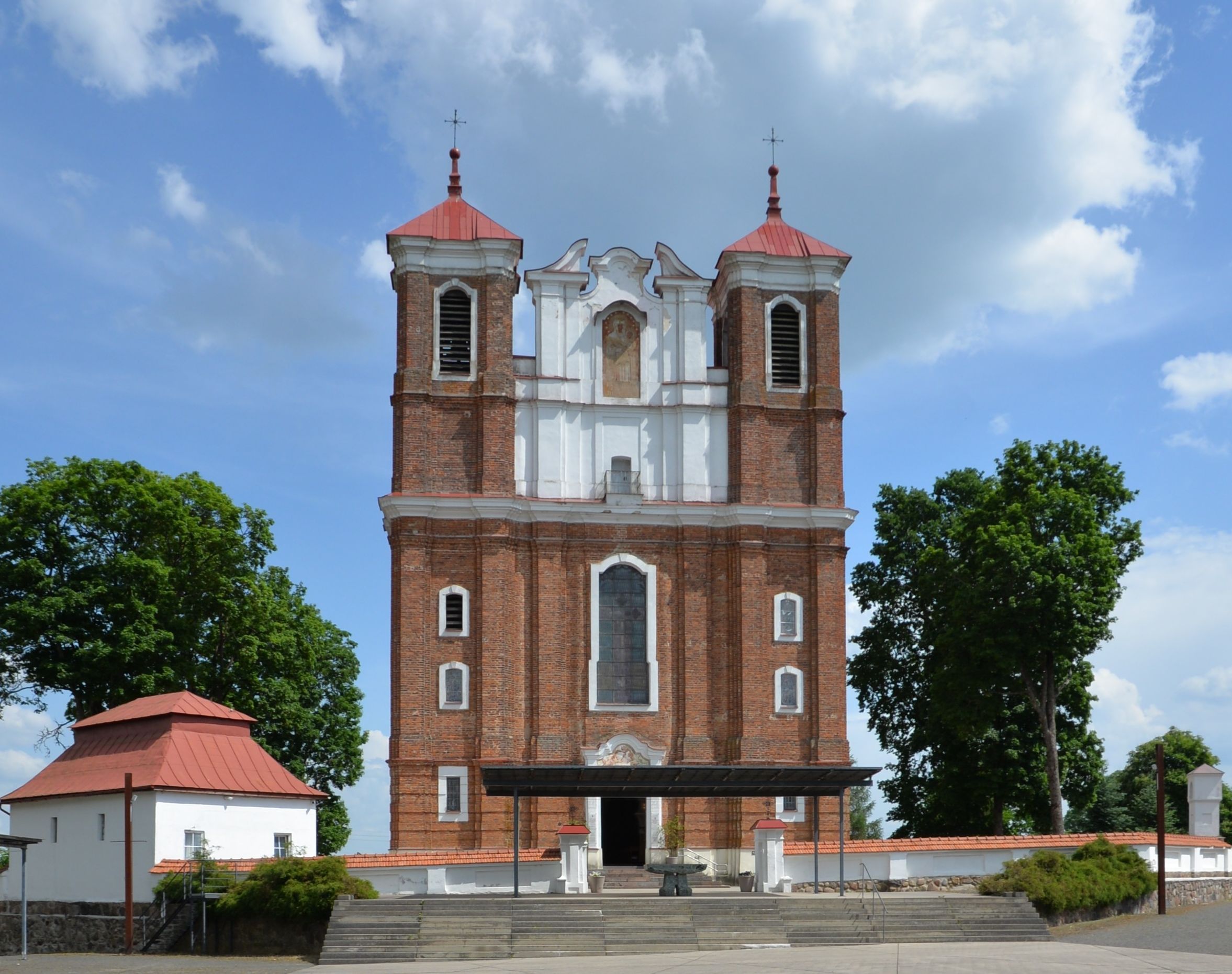 Façade de l'église de la Visitation de la Bienheureuse Vierge Marie à Szydłów, Lituanie, avec deux tours carrées et un haut fronton. L'église est en brique rouge avec des éléments plâtrés blancs.