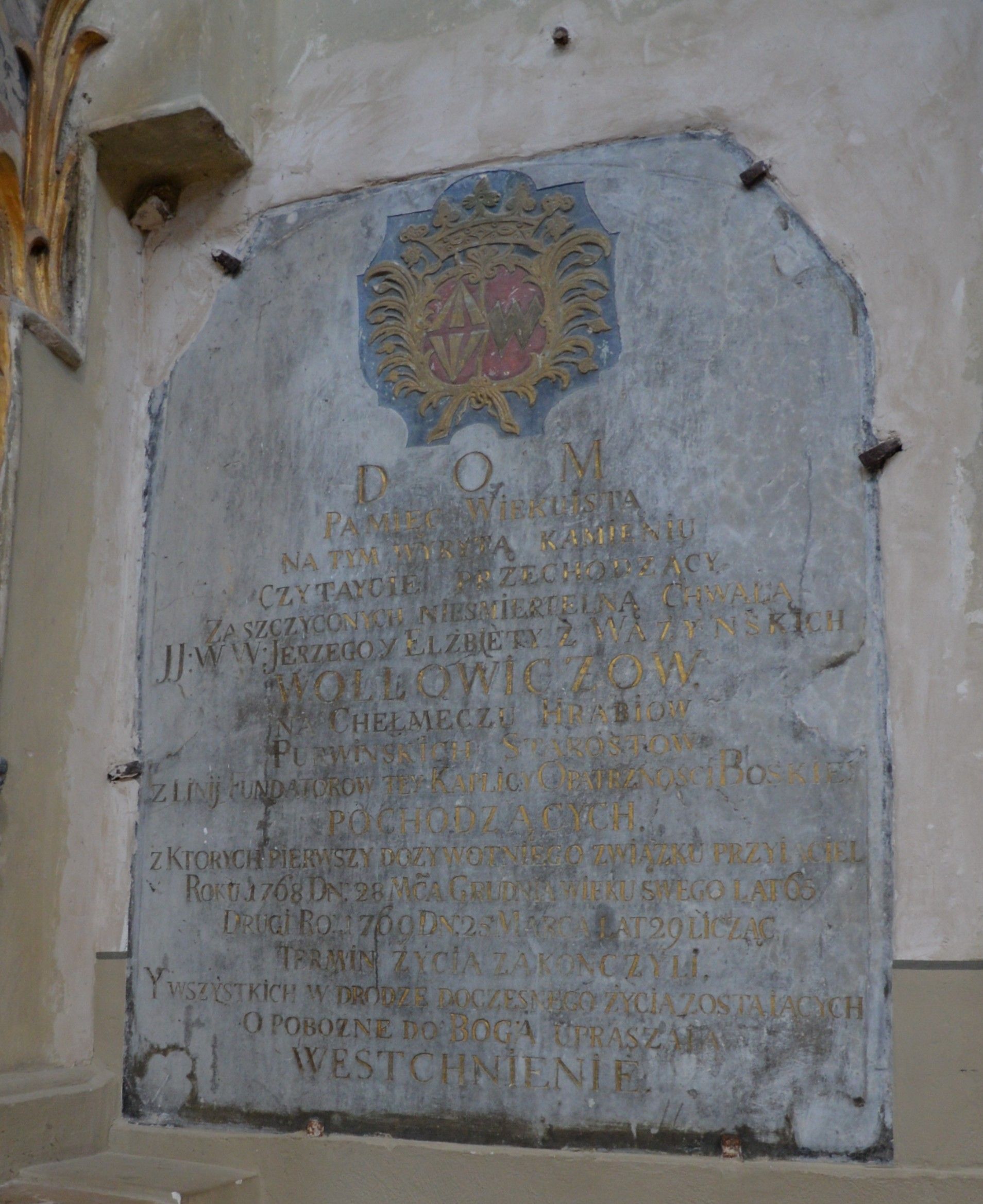 Stone plaque with an inscription in Polish, commemorating Jerzy and Elżbieta Wołłowicz, located in the Benedictine Church of St. Catherine in Vilnius. The plaque features a decorative coat of arms at the top.