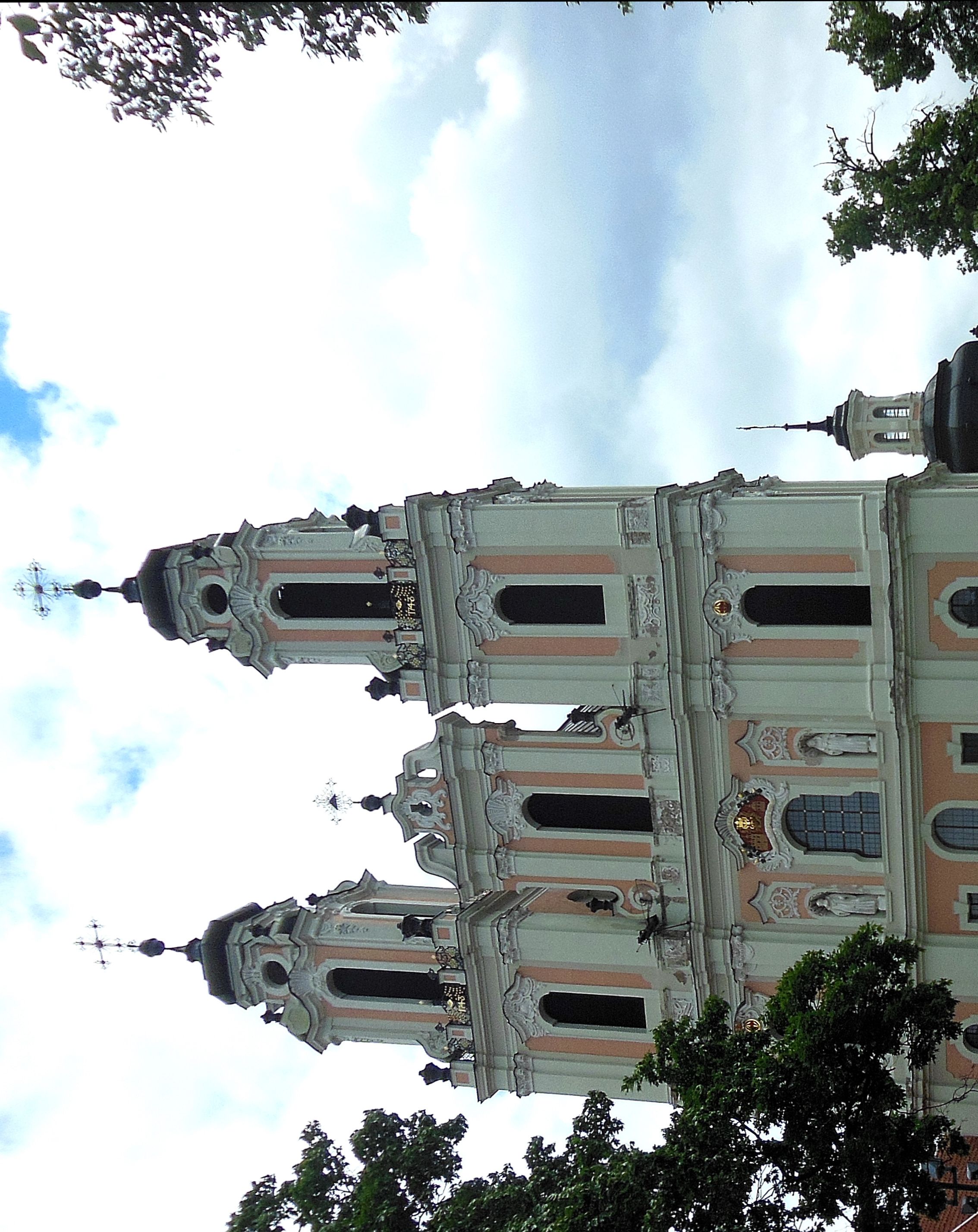 Facade of the Benedictine Church of St. Catherine in Vilnius with two five-story towers and decorative elements. Statues and architectural details are visible against a cloudy sky.