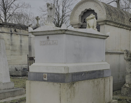 Nagrobek Bronisławy, Jean-Luca i Stefana Komadów z uskokowym cokołem, sarkofagiem i urną nakrytą całunem. Z przodu rzeźba anioła i napis 'Komada'.