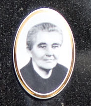 Black and white portrait of an elderly woman with short hair, wearing a dark top, set in an oval frame against a dark background.