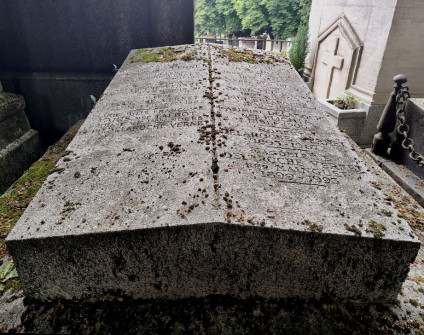 Nagrobek rodzin Delaroche i Plichta z dwuspadową płytą i rytymi inskrypcjami. Powyżej inskrypcji płytko ryte krzyże łacińskie. Na bokach metalowe uchwyty z motywem palmety.