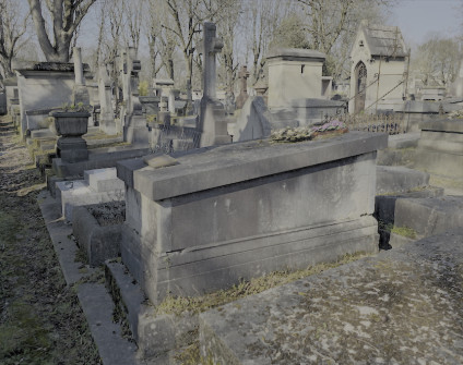 Nagrobek Eweliny i Marcelego Tąszewskich z cokolem schodkowym i skośną tumbą. Nad inskrypcjami wyryty mały krzyż. Grób otoczony innymi nagrobkami na cmentarzu.