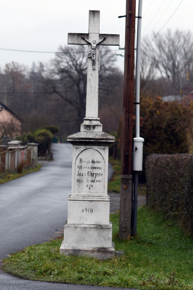 Roadside cross in the Czech part of Těšín Silesia, dated 1910. The inscription reads: 'Thou who art crucified for us, Jesus Christ, have mercy on us.' The cross stands on a stone plinth by a village road.