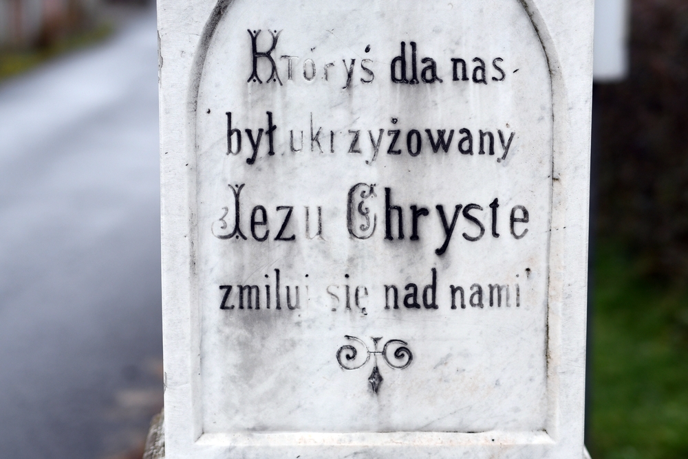 Close-up of the inscription on a roadside cross in Těšín Silesia, on the Czech side, with the inscription: 'Thou who art crucified for us, Jesus Christ, have mercy on us.' Text engraved on the stone tablet.