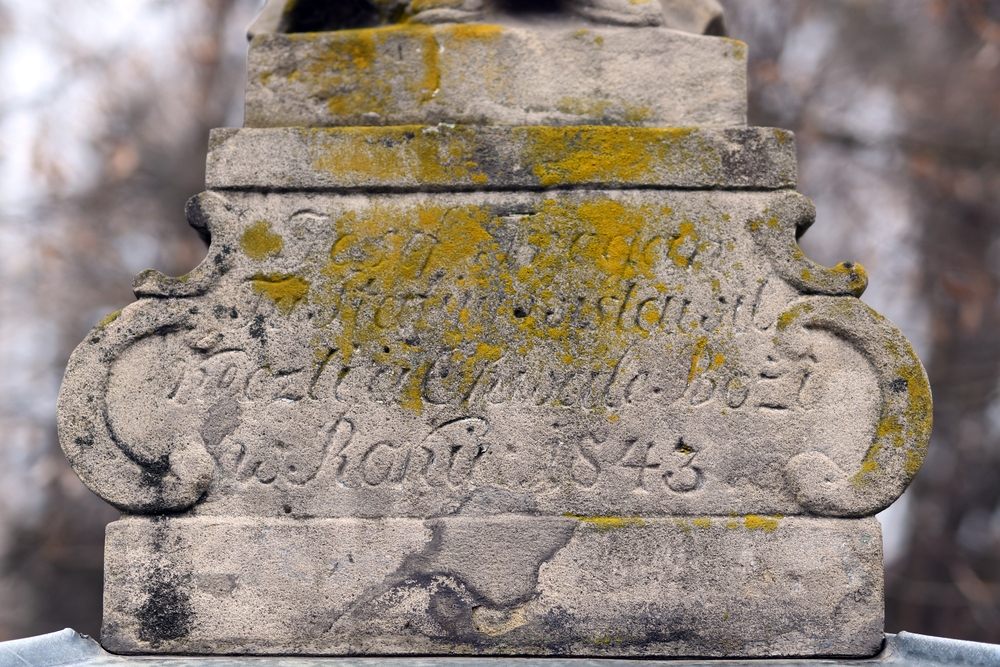 Close-up of a faded inscription on a stone religious monument in Těšín Silesia, Bohemia, partly covered with moss, dated 1843.