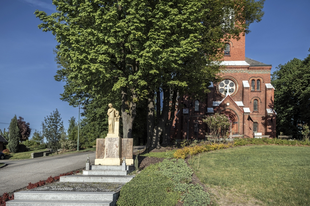 Пам'ятник Першій світовій війні перед цегляною церквою, оточеною деревами, у Карвіні, Чехія.