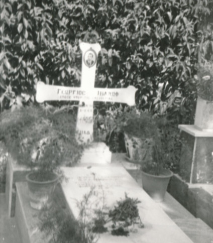 Grób Jerzego Iwanowa-Szajnowicza w Atenach, z marmurowym krzyżem z grecką inskrypcją i zdjęciem zmarłego. Grób ozdobiony roślinami i polską inskrypcją na płycie.
