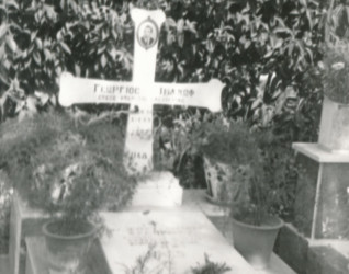 Grób Jerzego Iwanowa-Szajnowicza w Atenach, z marmurowym krzyżem z grecką inskrypcją i zdjęciem zmarłego. Grób ozdobiony roślinami i polską inskrypcją na płycie.