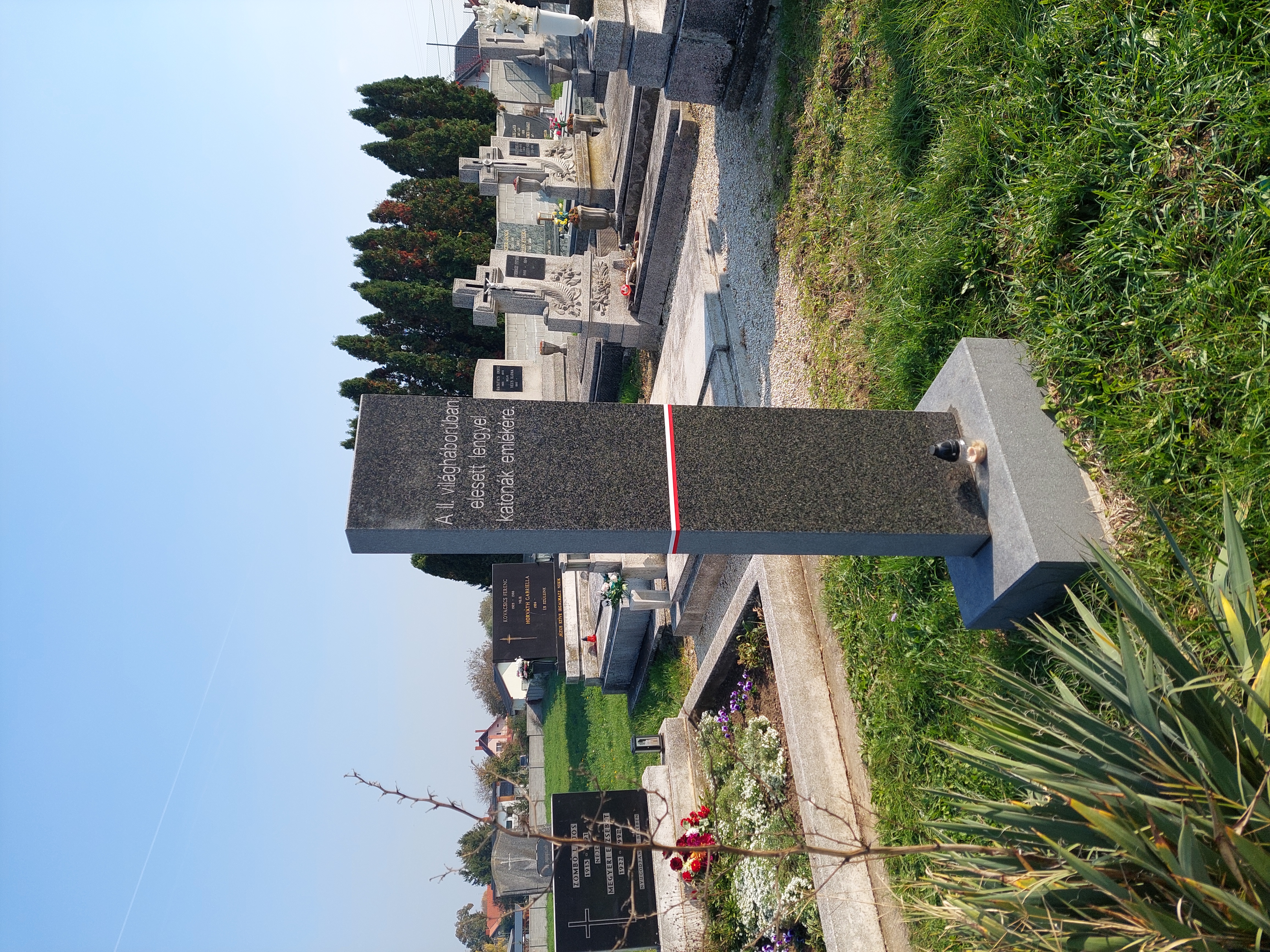Granite obelisk on a cemetery in Fertőszentmiklós, Hungary, commemorating Polish soldiers who died during World War II. Surrounding graves and trees are visible in the background.