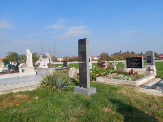 Groby polskich żołnierzy na cmentarzu w Fertőszentmiklós. Ciemny granitowy obelisk z węgierską inskrypcją stoi wśród grobów, otoczony zielenią i kwiatami.