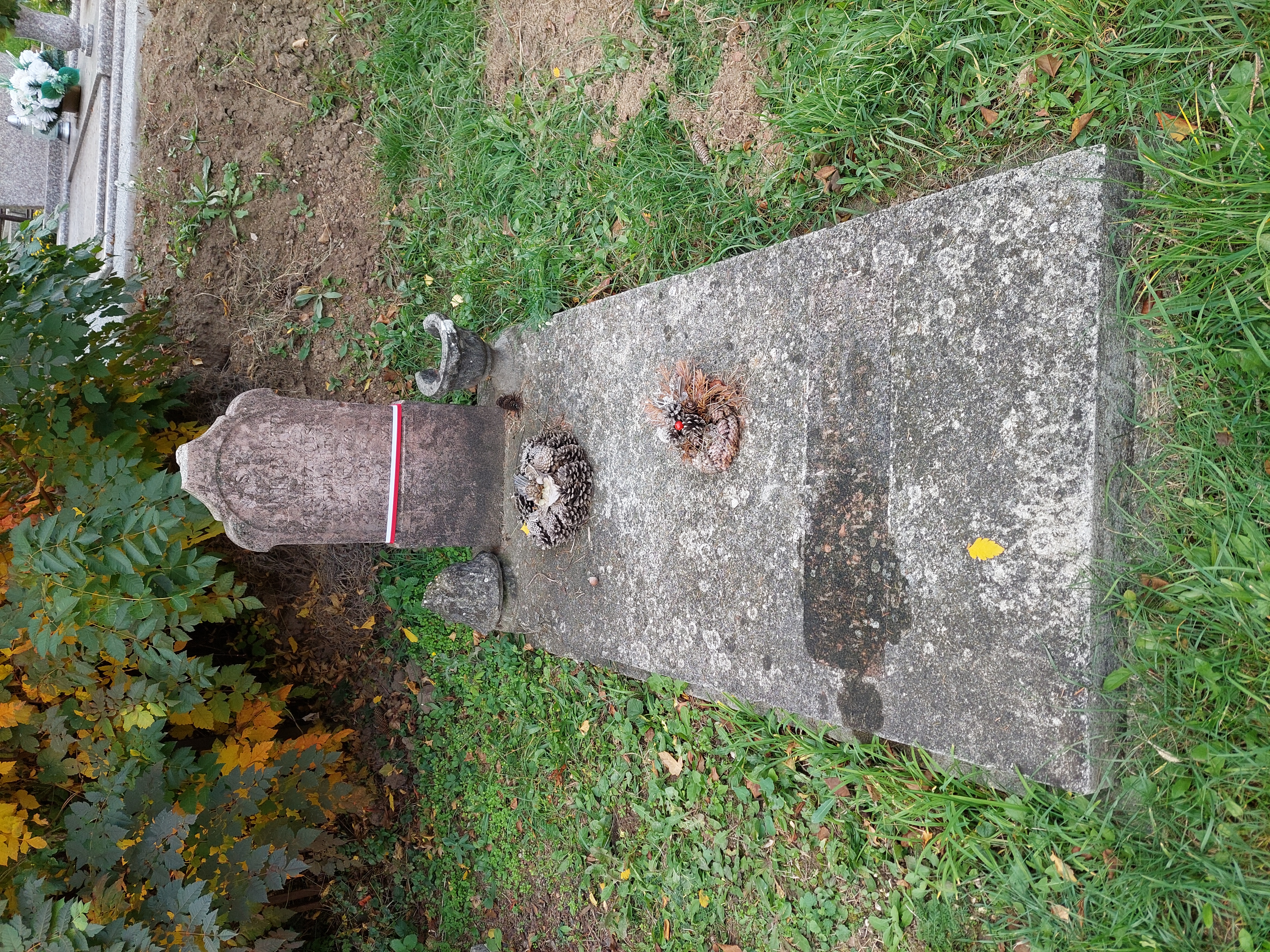 Grave of Polish soldier Piotr Kania in Lábatlan cemetery. The stone headstone bears inscriptions in Polish and Hungarian. A small wreath lies on the horizontal slab surrounded by grass and trees.