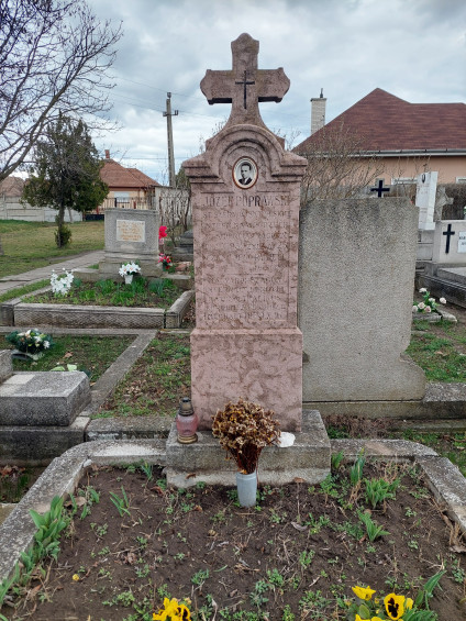 Grób Józefa Poprawskiego, polskiego żołnierza, z różową kamienną tablicą zwieńczoną krzyżem. Inskrypcja zawiera jego imię i szczegóły. Wbudowane jest jego zdjęcie. Przed grobem stoi znicz i suche kwiaty.