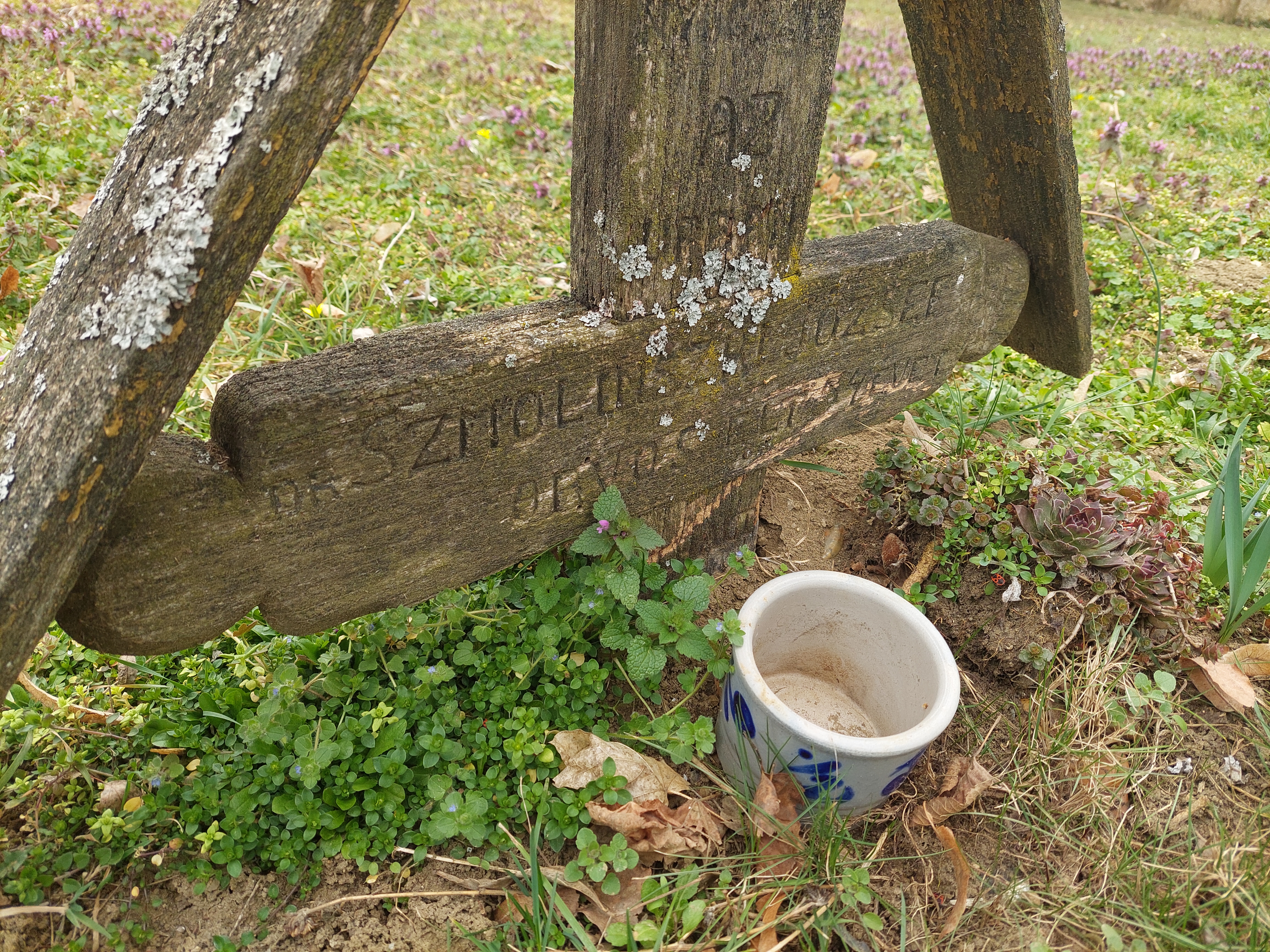 Croix en bois sur la tombe du réfugié polonais Józef Smoliński à Oroszi, Hongrie. La croix porte une inscription hongroise partiellement effacée. Un petit pot en céramique est placé à la base.