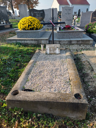 Grób polskiego żołnierza Edwarda Drozdowskiego z metalowym krzyżem i dwujęzyczną tablicą. Grób otoczony innymi nagrobkami i żółtym krzewem chryzantem.