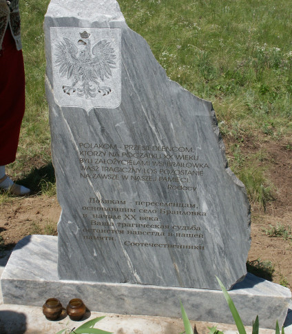 Kamienny pomnik z polskimi i rosyjskimi inskrypcjami upamiętniający polskich osadników wsi Braiłowka, z wyrytym godłem orła. Dwa znicze u podstawy, otoczone trawą.