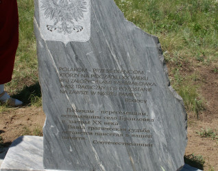 Kamienny pomnik z polskimi i rosyjskimi inskrypcjami upamiętniający polskich osadników wsi Braiłowka, z wyrytym godłem orła. Dwa znicze u podstawy, otoczone trawą.