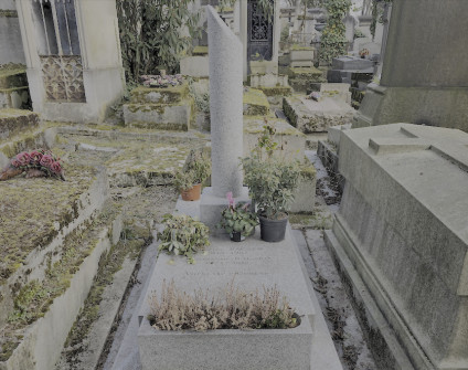 Nagrobek rodzin Baczków i Zakrzewskich z wysokim cokołem, złamaną kolumną i inskrypcjami. Wokół nagrobka ustawione są rośliny i kwiaty w doniczkach.