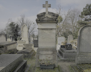 Nagrobek Kacpra i Marie Saskich z cokółem schodkowym i krzyżem na szczycie. Inskrypcja na froncie. Otoczony innymi nagrobkami na cmentarzu.