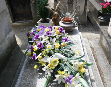 Nagrobek Huguette Brzezińskiej i Louisa Marouby z płaską, lekko skośną płytą na wysokim cokole. Na płycie leży kompozycja kwiatowa z białych lilii, żółtych róż i fioletowych kwiatów.