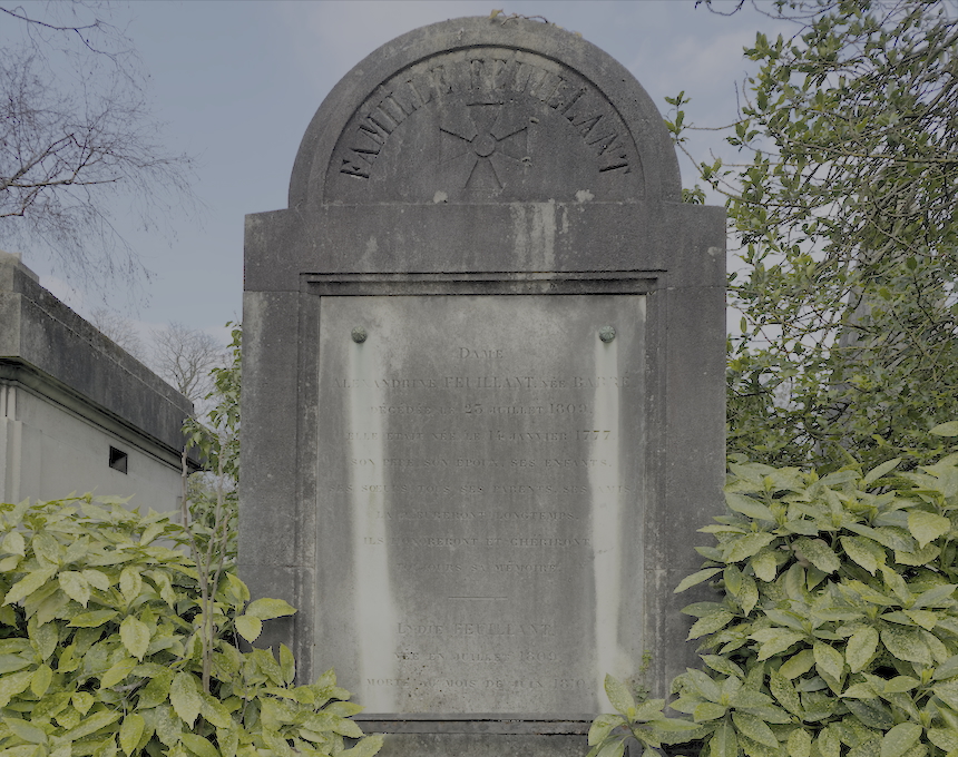 Pierre tombale de la famille Feuillant avec un sommet semi-circulaire et des inscriptions gravées. Entourée de verdure, la pierre présente un relief de croix et le nom 'FAMILLE FEUILLANT'.