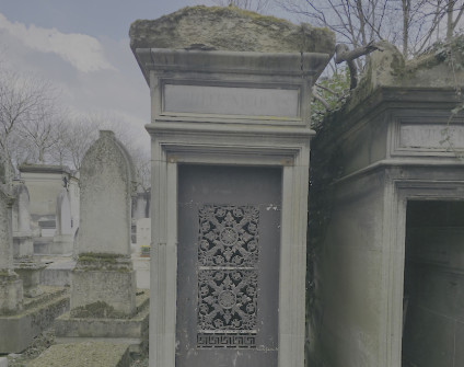 Kamienna kapliczka z dwuspadowym dachem, z misterną metaloplastyką na drzwiach. Wokół inne kamienne struktury i bezlistne drzewa.