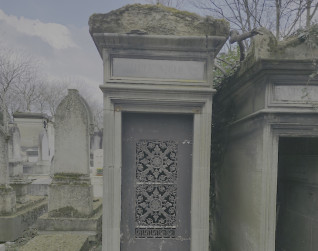 Kamienna kapliczka z dwuspadowym dachem, z misterną metaloplastyką na drzwiach. Wokół inne kamienne struktury i bezlistne drzewa.