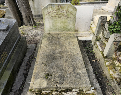 Nagrobek Natana Szlezyngera z prostokątną stelą z inskrypcją. Dwa pierwsze wersy tekstu ułożone na łuku. Grób znajduje się na cmentarzu otoczonym zielenią.