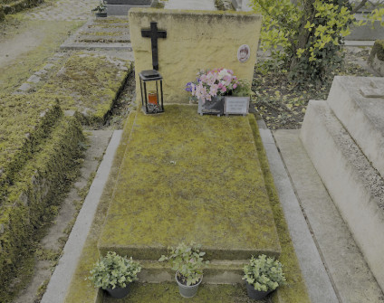 Nagrobek Elżbiety Kuczek z czarnym marmurowym krzyżem, fotografią na porcelanie i inskrypcjami. Na pokrytej mchem płycie znajdują się kwiaty i latarnia.