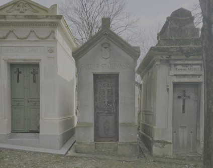 Kapliczka z trójkątnym dachem i napisem 'Famille Starzynski' nad drzwiami. Dekoracyjne drzwi żeliwne z motywami krzyża. Sąsiednie kapliczki w podobnym stylu architektonicznym.