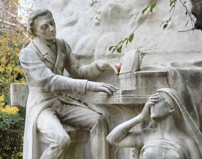 Rzeźba Fryderyka Chopina w paryskim Parku Monceau, ukazująca Chopina siedzącego przy fortepianie z kobietą symbolizującą Słuch u jego stóp, zasłaniającą oczy. Wokół rzeźby widoczne liście i gałęzie.