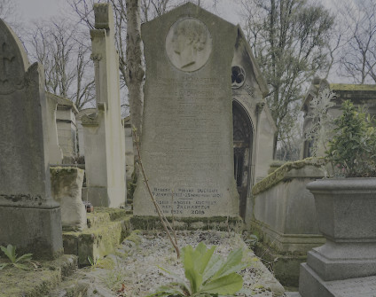 Nagrobek rodziny Zacharezuków z wysoką stelą o trójkątnym zakończeniu i reliefem kobiecego profilu. Widoczna inskrypcja na steli. Otaczające groby i roślinność.