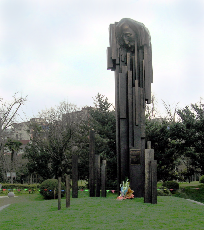 Statue en bronze de Frédéric Chopin dans le parc Zhongshan de Shanghai. Une sculpture abstraite avec des colonnes verticales ressemblant à des touches de piano, avec le profil de Chopin émergeant. La sculpture est entourée d'arbres et d'herbe.