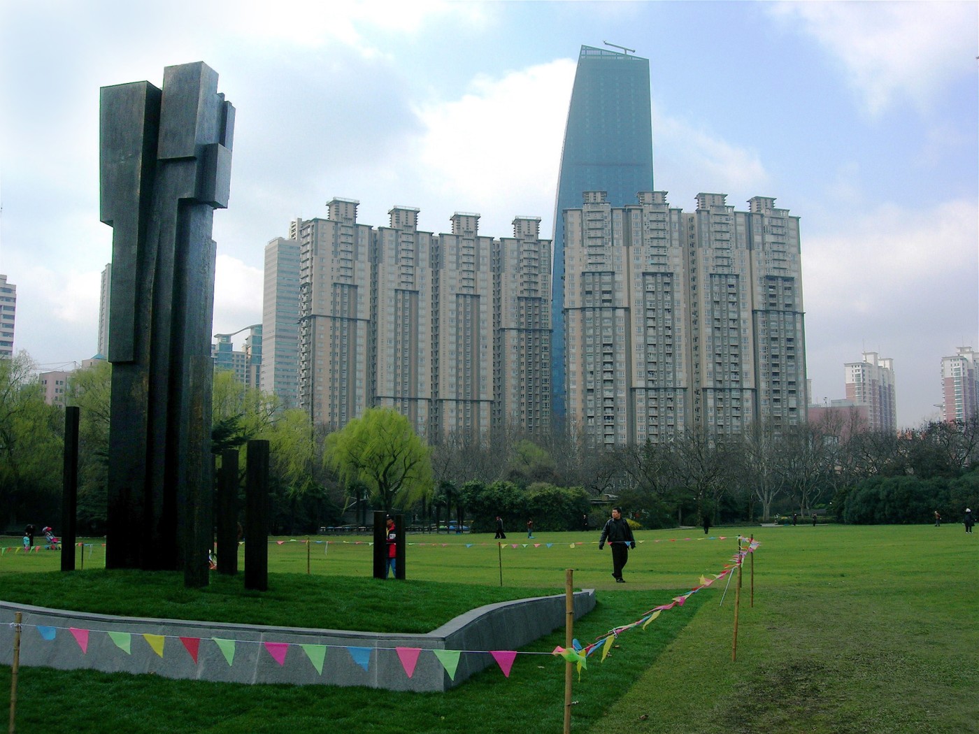 Monument à Frédéric Chopin dans le parc Zhongshan de Shanghai avec des colonnes verticales abstraites ressemblant à des touches de piano. En arrière-plan, de grands bâtiments modernes sur fond de ciel nuageux.