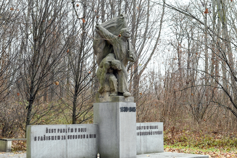 Пам'ятник у Карвіні-Рай, що вшановує жертв Другої світової війни, з скульптурою двох фігур та написами чеською і польською мовами. На задньому плані дерева без листя.