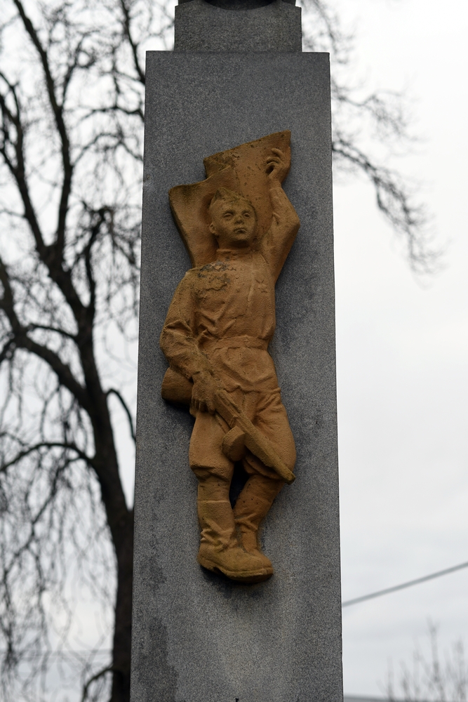 Кам'яний пам'ятник у Петровицях біля Карвіни з рельєфом дитини, що тримає прапор і інструмент, на тлі голих дерев.