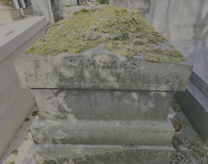 Kamienny nagrobek z cokołem schodkowym i pokrytym mchem dwuspadowym wierzchem, z wyrytym napisem 'FAMILLES PROTAT ET DUTILLOY'. Po bokach widoczne metalowe haki na wieńce.
