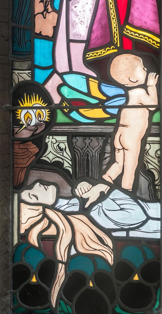 Jozef Mehoffer's stained glass window in the Grauer family chapel in Opava, depicting a dead woman with flowing hair and a child with coloured wings symbolising the soul. Dark pansies and a candle are visible below.