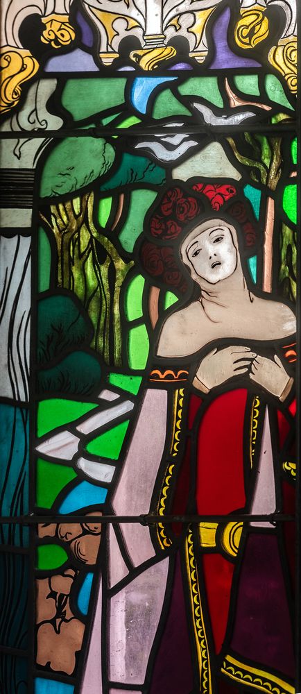 Stained glass window by Jozef Mehoffer in the Grauer family chapel in Opava, depicting a woman in a red dress with a floral headdress, surrounded by trees and vivid colours.