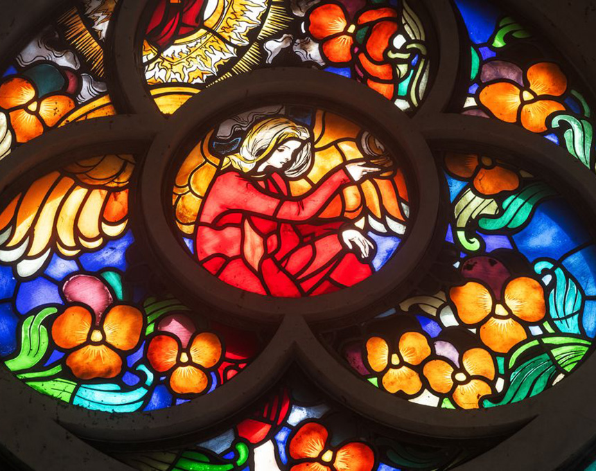 Jozef Mehoffer's stained glass window in the Grauer family chapel in Opava, depicting an angel in red robes surrounded by vivid floral motifs in shades of orange, blue and green.