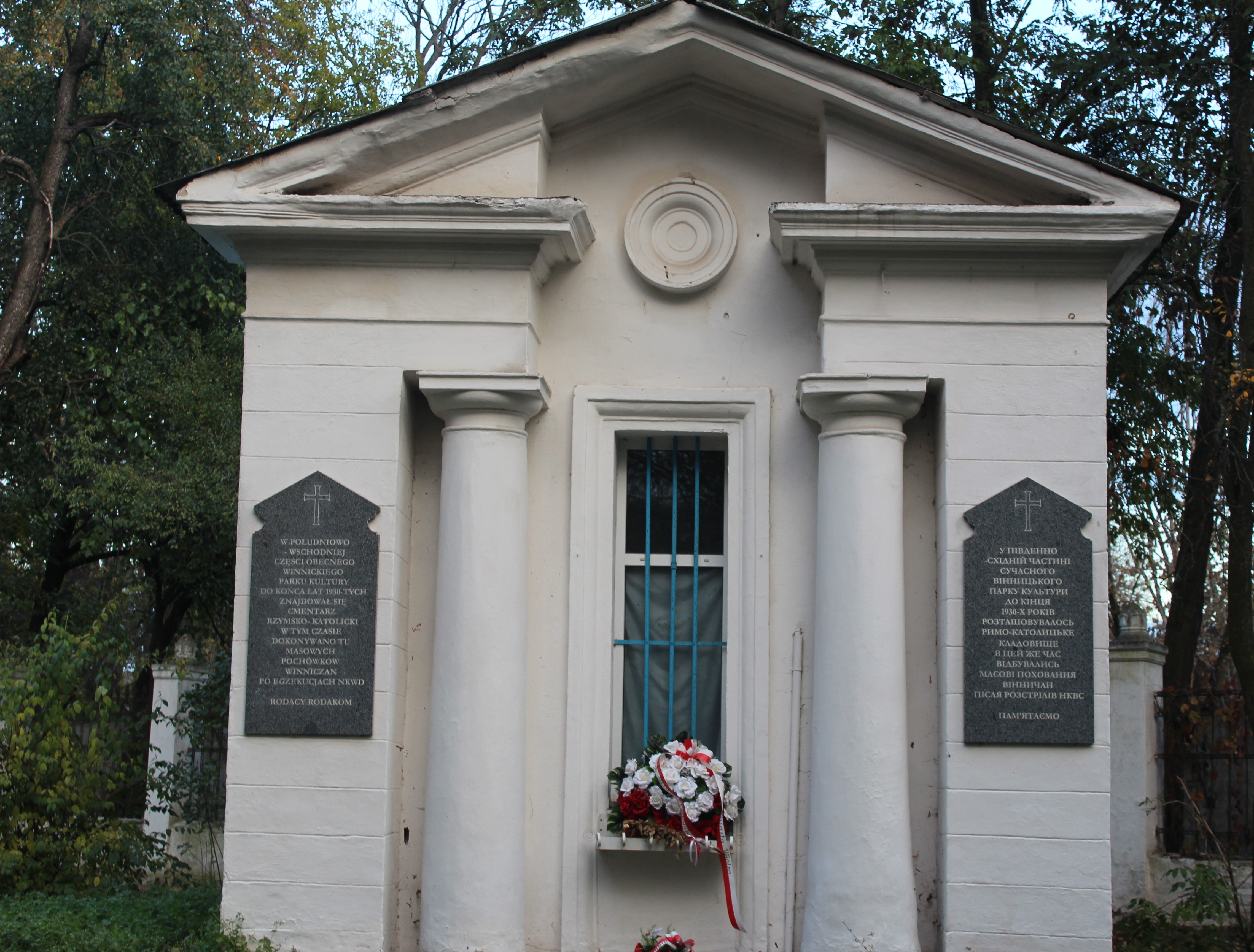 Chapelle dans le parc central de Vinnytsia avec deux plaques commémoratives sur le mur avant et une couronne de fleurs sous une fenêtre grillagée.
