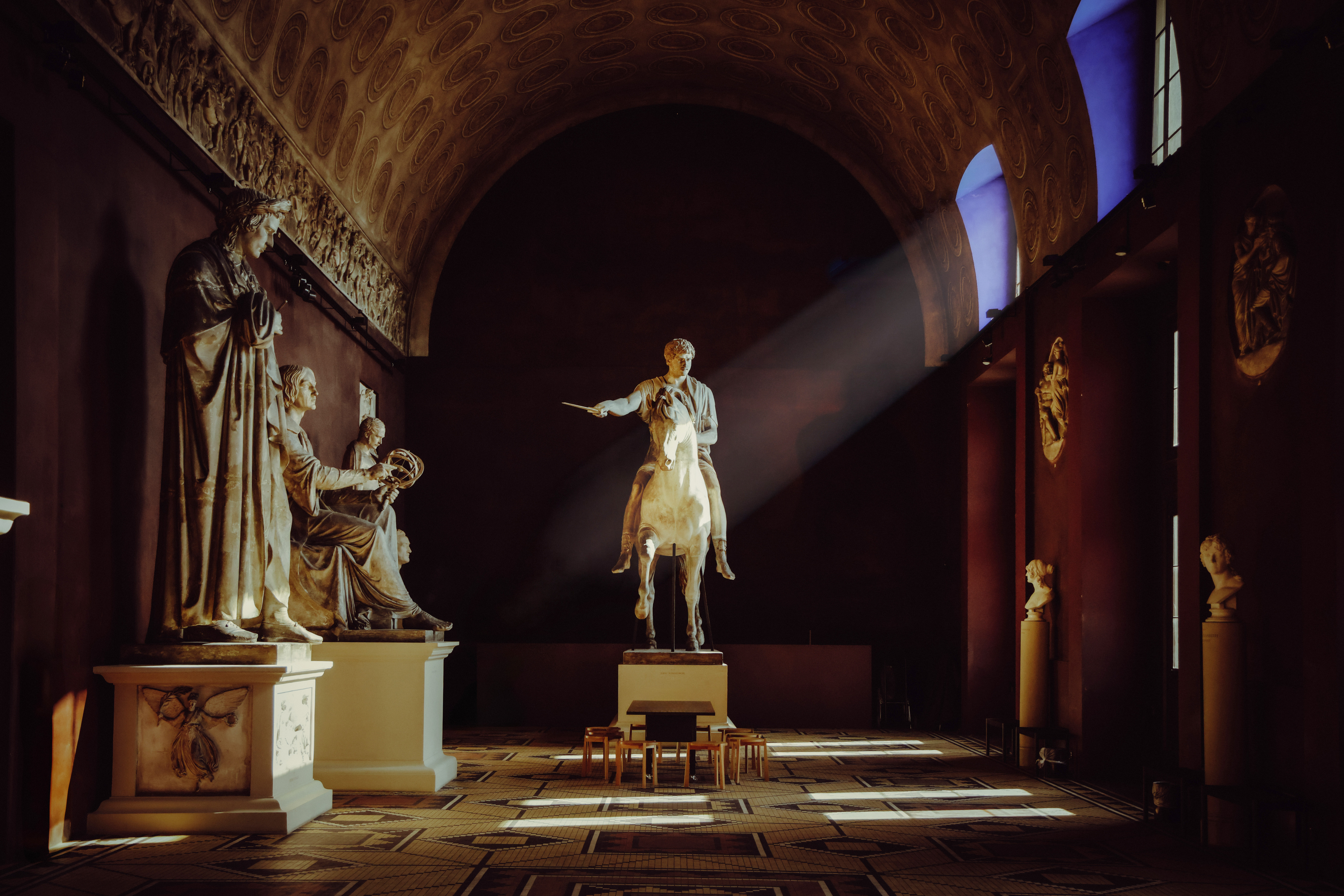 Plaster casts of Prince Józef Poniatowski and Nicolaus Copernicus statues in Bertel Thorvaldsen Museum, Copenhagen. The room is dimly lit with sunlight streaming through windows.