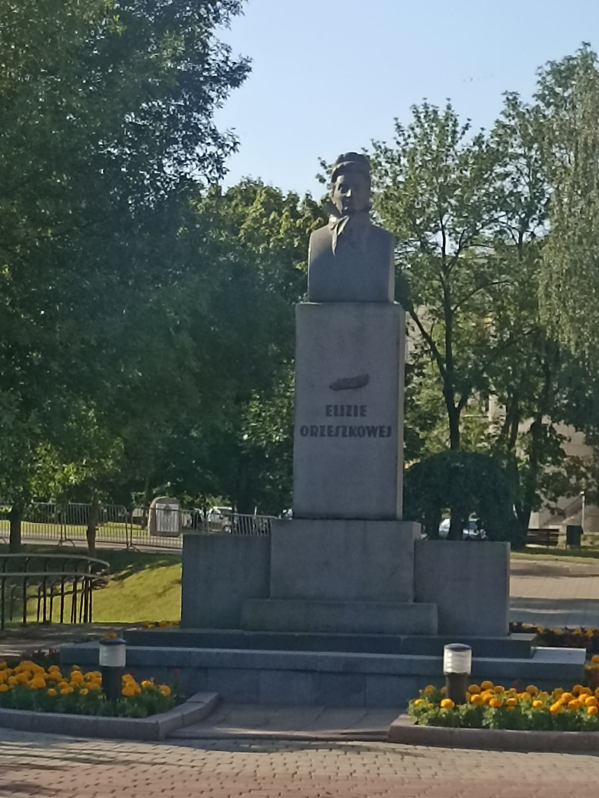 Popiersie Elizy Orzeszkowej na cokole z jej imieniem, otoczone drzewami i kwiatami w Grodnie.