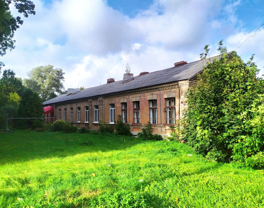 Historic building in Baranowicze, formerly housing the headquarters of the Nowogródek Cavalry Brigade, with a long, single-story structure, brick facade, and surrounded by greenery.