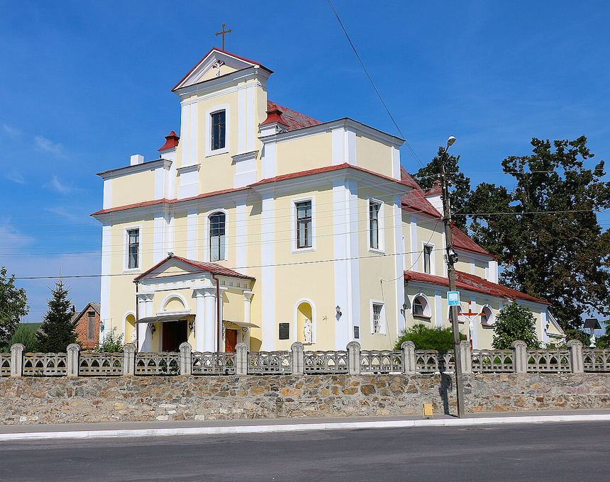 Церква Святої Трійці в Хмільнику, жовто-біла барокова будівля з червоним дахом, оточена кам'яним парканом.