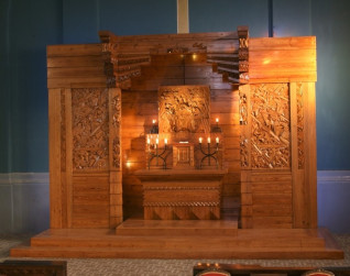 Drewniany ołtarz z misternymi rzeźbieniami, przedstawiający motywy religijne, oświetlony światłem świec. Ołtarz jest częścią polskiej ekspozycji na Międzynarodowej Wystawie Sztuk Dekoracyjnych i Przemysłu w Paryżu w 1925 roku.