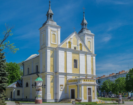 Fotografia kościoła świętych Joachima i Anny we Włodzimierzu Wołyńskim z żółto białą fasadą i dwiema wieżami zwieńczonymi krzyżami
