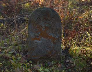 Zniszczony kamienny słupek graniczny w Krompachach z datą 1755, z dwoma młotami górniczymi i literami KR, otoczony trawą i jesiennym listowiem.