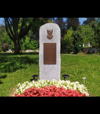 Granitowy obelisk z tablicą upamiętniającą żołnierzy 2. Dywizji Strzelców, otoczony kwiatami i zielenią na cmentarzu.